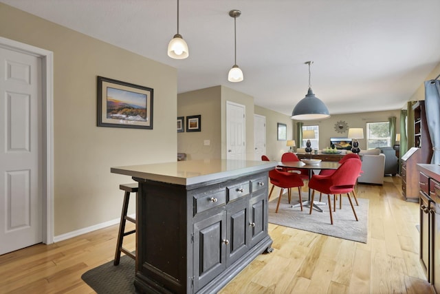 kitchen featuring pendant lighting, light wood-style floors, baseboards, a kitchen bar, and light countertops