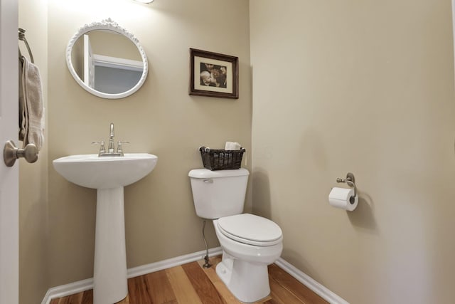 half bathroom with toilet, baseboards, a sink, and wood finished floors
