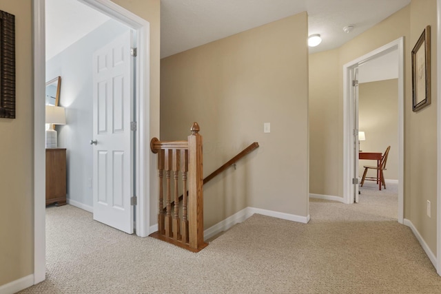 hallway featuring baseboards, carpet flooring, and an upstairs landing