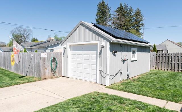 detached garage with fence, driveway, and roof mounted solar panels