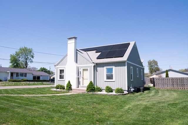 view of front of home featuring board and batten siding, a chimney, solar panels, and a front yard