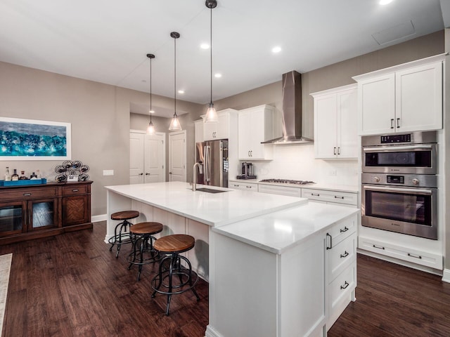 kitchen featuring a spacious island, dark wood-type flooring, wall chimney exhaust hood, a sink, and stainless steel appliances