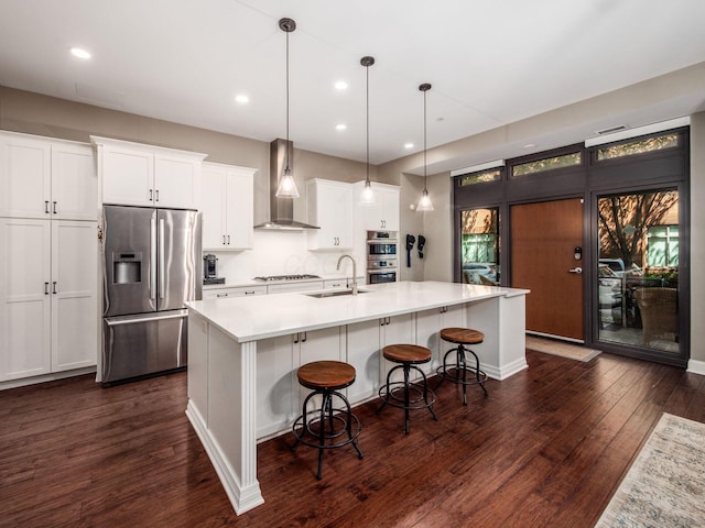 kitchen with wall chimney range hood, white cabinets, light countertops, stainless steel appliances, and dark wood-style floors