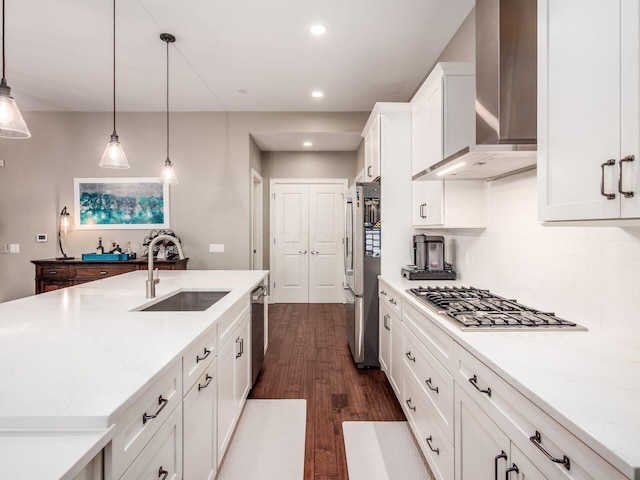 kitchen featuring wall chimney range hood, white cabinets, appliances with stainless steel finishes, a sink, and dark wood finished floors