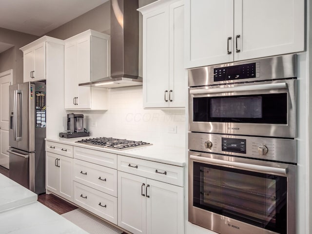 kitchen with decorative backsplash, white cabinetry, wall chimney range hood, and stainless steel appliances