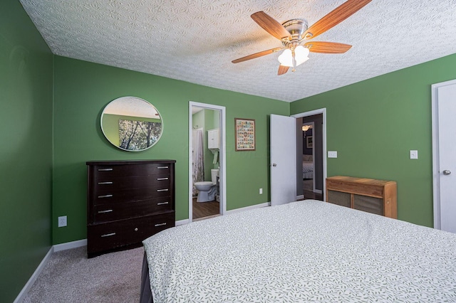 bedroom featuring ceiling fan, a textured ceiling, carpet floors, baseboards, and ensuite bathroom