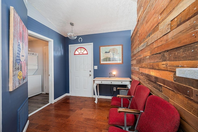 entrance foyer with a textured ceiling, stacked washer / drying machine, wood finished floors, baseboards, and lofted ceiling