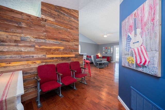 living area with visible vents, a textured ceiling, wood finished floors, and vaulted ceiling