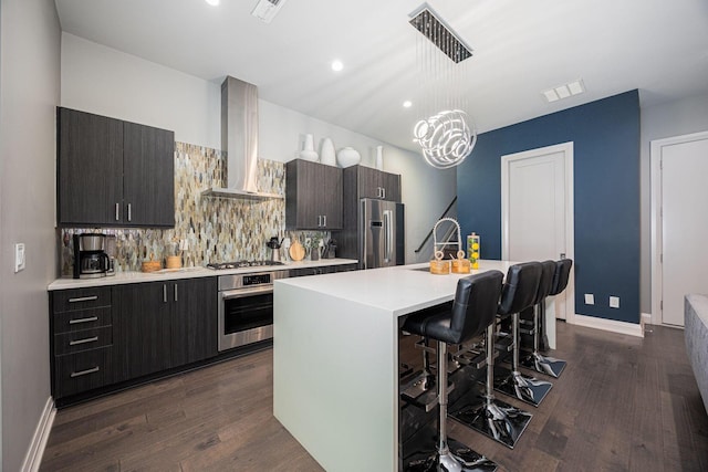 kitchen with wall chimney range hood, a breakfast bar area, appliances with stainless steel finishes, tasteful backsplash, and light countertops