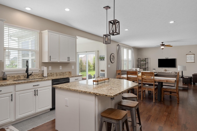 kitchen featuring a ceiling fan, a center island, dishwasher, a sink, and white cabinets