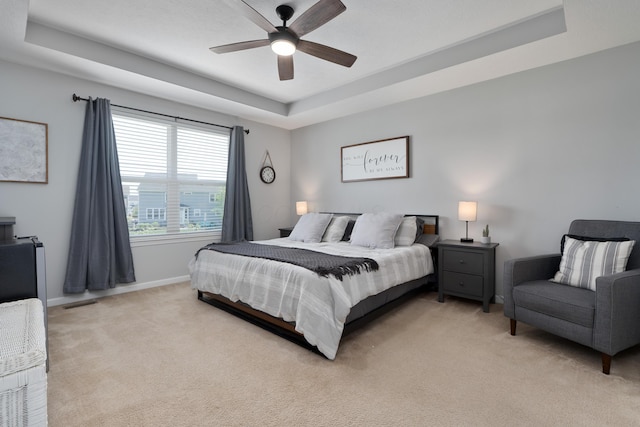bedroom featuring a ceiling fan, visible vents, a raised ceiling, baseboards, and light carpet