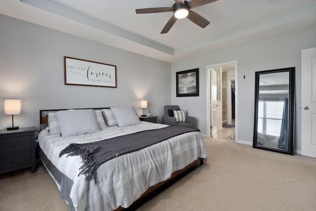 carpeted bedroom with baseboards, ceiling fan, a tray ceiling, and ensuite bath