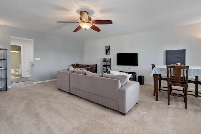 living area featuring baseboards, light carpet, and a ceiling fan