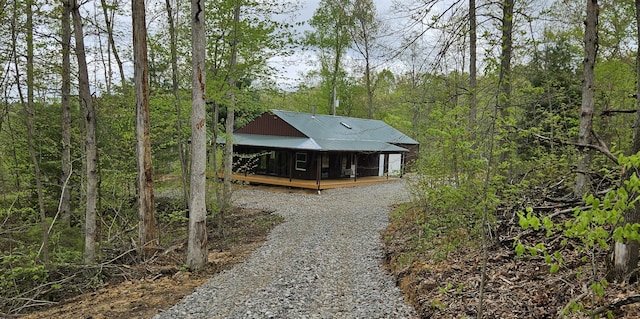 exterior space featuring covered porch, driveway, a forest view, and metal roof
