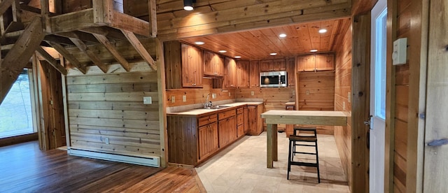 kitchen with a baseboard radiator, a sink, stainless steel microwave, wooden walls, and brown cabinets
