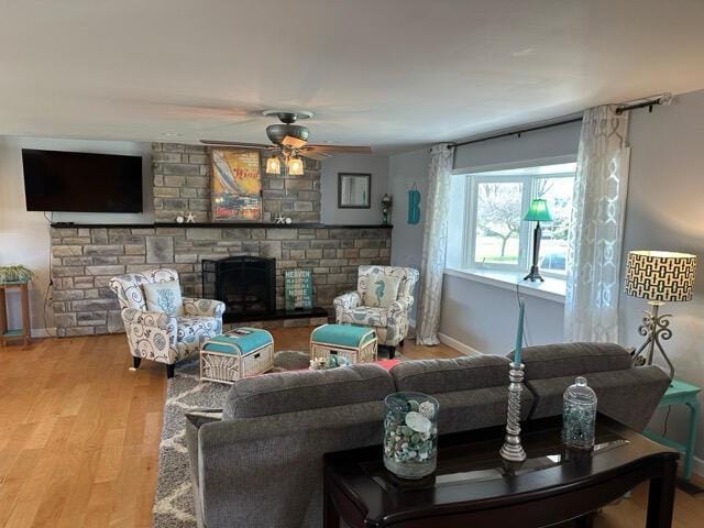 living area featuring baseboards, a ceiling fan, wood finished floors, and a fireplace