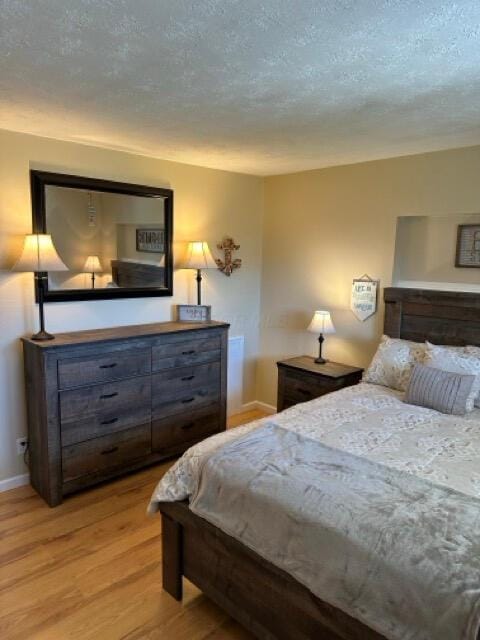 bedroom featuring baseboards, a textured ceiling, and light wood-style flooring