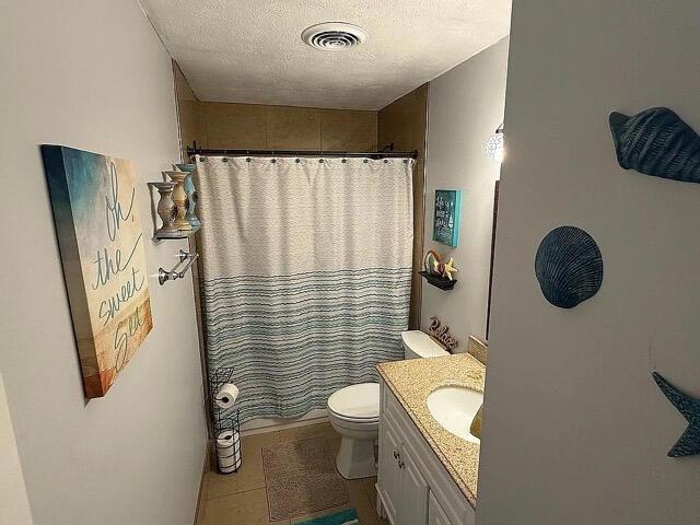 full bath with vanity, toilet, a textured ceiling, curtained shower, and visible vents