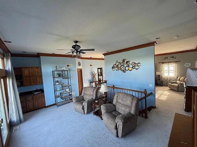 living area with crown molding, a ceiling fan, visible vents, and light carpet