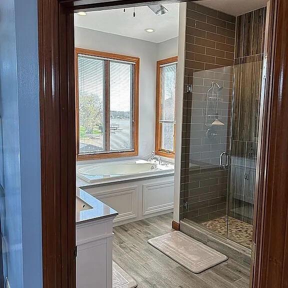 full bathroom with vanity, a bath, a shower stall, and wood finished floors