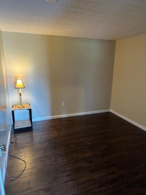 empty room featuring a textured ceiling, baseboards, and wood finished floors