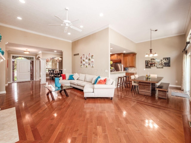 living room with light wood finished floors, crown molding, ornate columns, and ceiling fan with notable chandelier