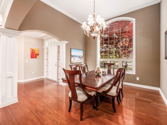 dining area featuring arched walkways, ornamental molding, a chandelier, and wood finished floors