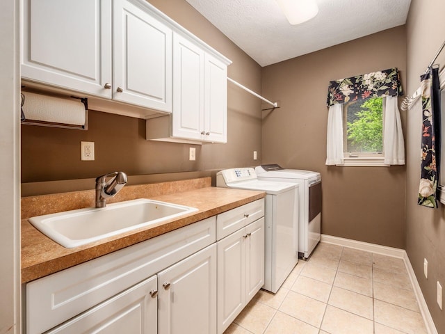 clothes washing area featuring washer and dryer, light tile patterned floors, a sink, cabinet space, and baseboards