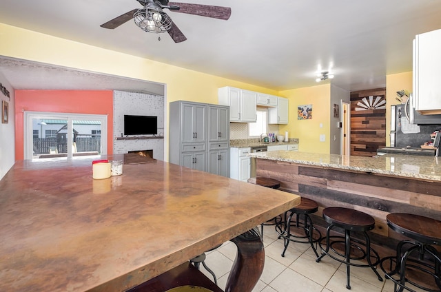 kitchen with ceiling fan, light stone counters, stove, light tile patterned floors, and tasteful backsplash