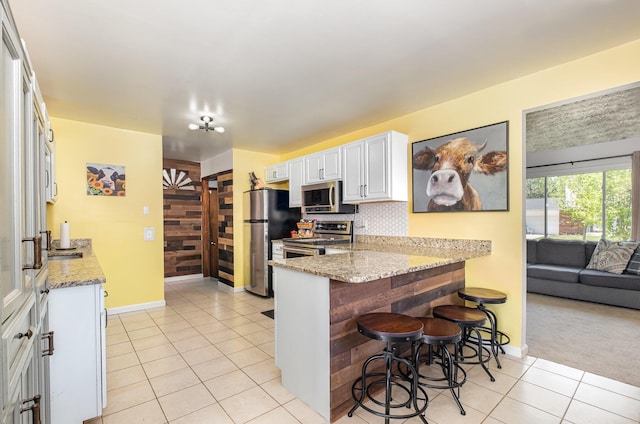 kitchen featuring appliances with stainless steel finishes, light tile patterned floors, baseboards, light stone counters, and a peninsula
