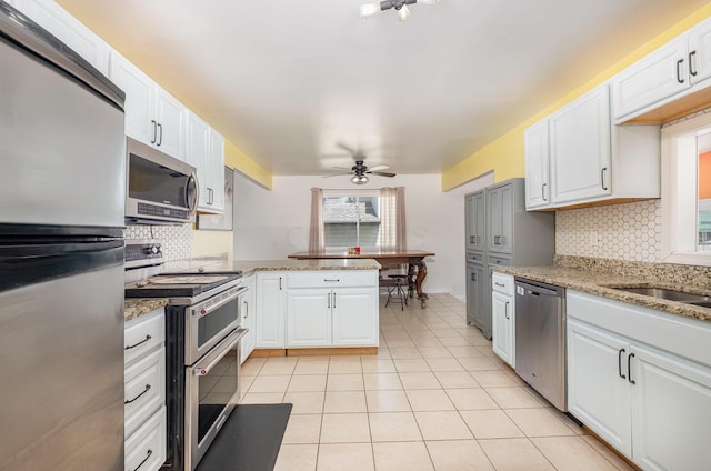 kitchen with decorative backsplash, a peninsula, a ceiling fan, light tile patterned floors, and stainless steel appliances