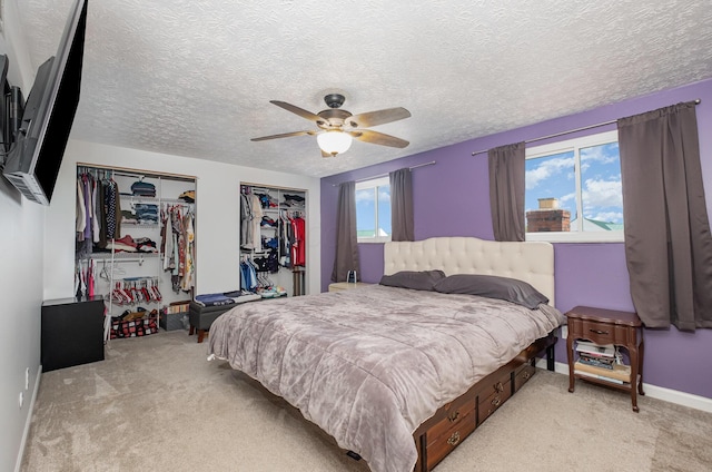 carpeted bedroom with a ceiling fan, a textured ceiling, and two closets