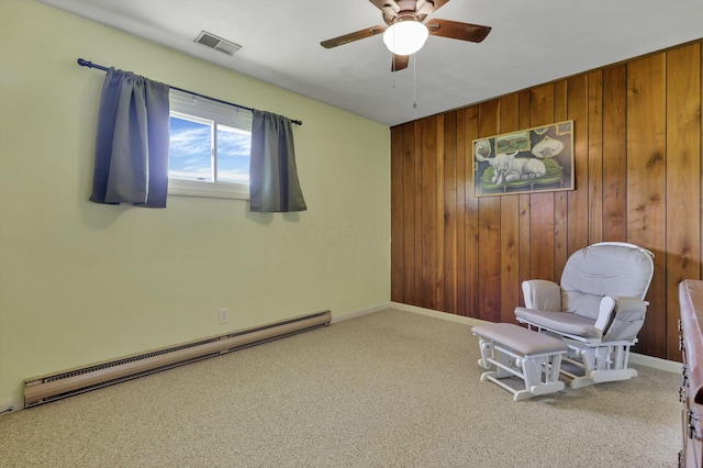sitting room with a ceiling fan, visible vents, wood walls, carpet floors, and a baseboard heating unit