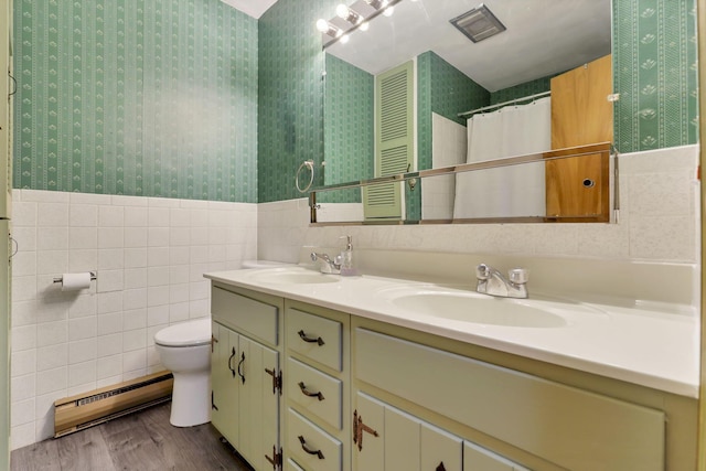 bathroom featuring double vanity, a sink, tile walls, wallpapered walls, and a baseboard radiator
