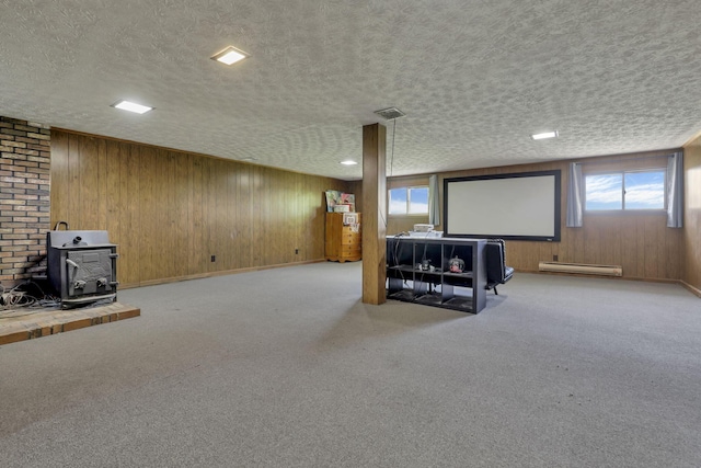 basement featuring a baseboard radiator, a wood stove, a textured ceiling, and a wealth of natural light