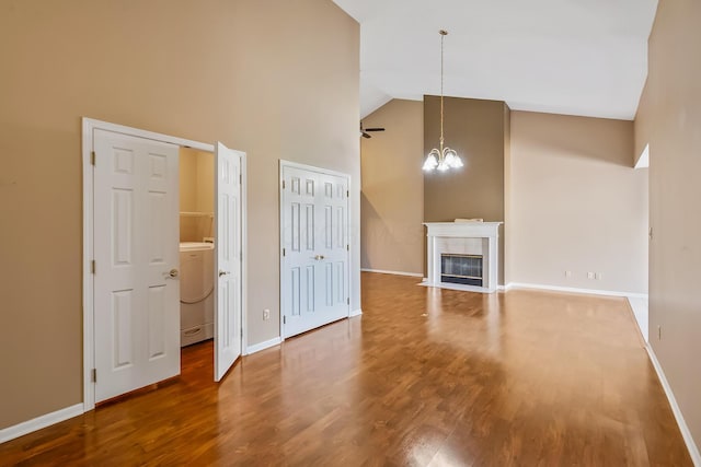 unfurnished living room with washer / dryer, high vaulted ceiling, wood finished floors, and a chandelier