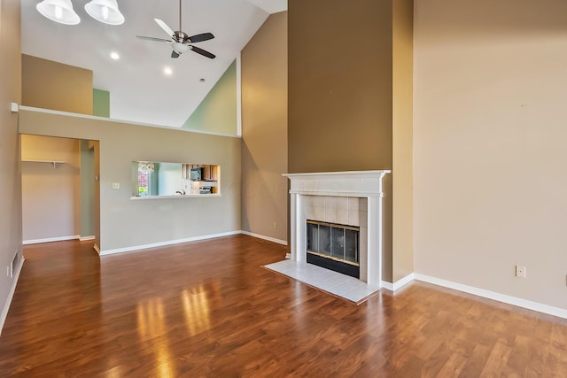 unfurnished living room with high vaulted ceiling, a ceiling fan, a tile fireplace, and wood finished floors