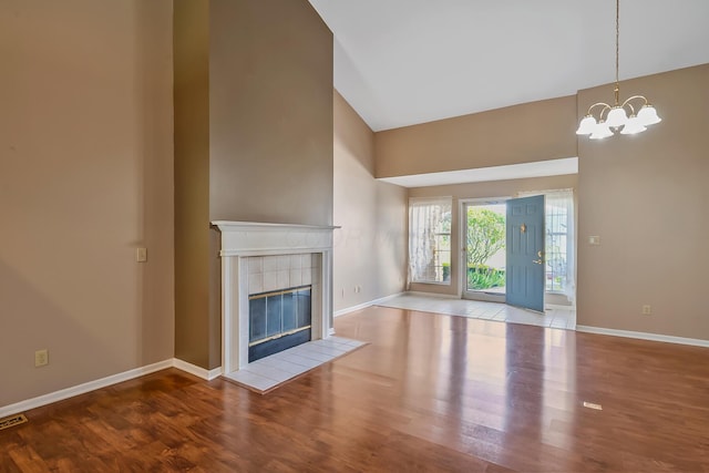 unfurnished living room featuring baseboards, a notable chandelier, wood finished floors, and a towering ceiling