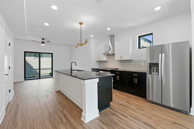 kitchen featuring dark countertops, wall chimney range hood, plenty of natural light, a sink, and appliances with stainless steel finishes