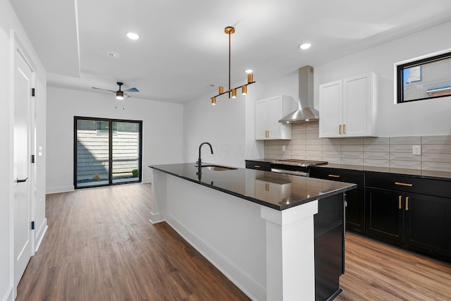 kitchen featuring wall chimney range hood, dark countertops, a sink, and wood finished floors
