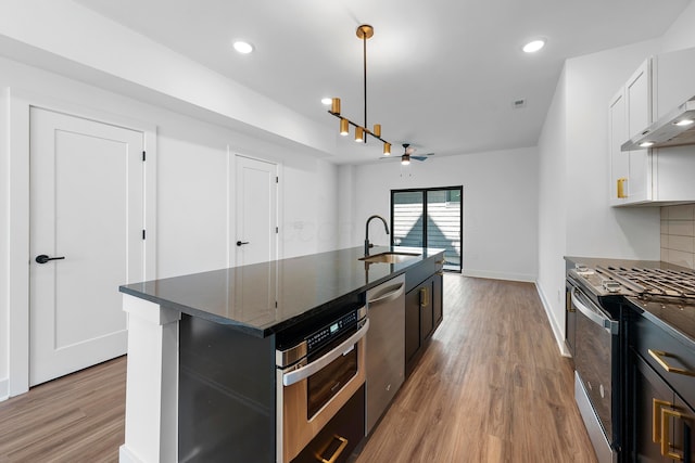 kitchen featuring ceiling fan, a center island with sink, a sink, light wood-style flooring, and stainless steel appliances