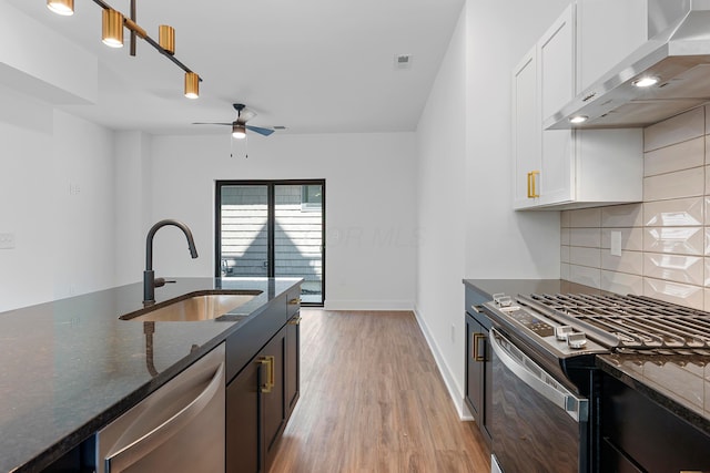 kitchen with decorative backsplash, wall chimney exhaust hood, a sink, dark stone countertops, and appliances with stainless steel finishes