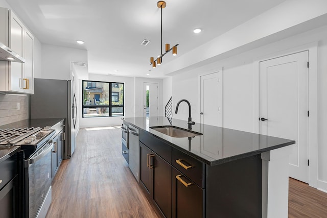kitchen with appliances with stainless steel finishes, a sink, recessed lighting, wood finished floors, and tasteful backsplash