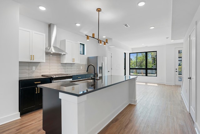 kitchen with wall chimney range hood, dark countertops, light wood-type flooring, a sink, and stainless steel fridge