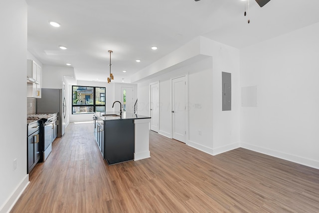 kitchen with ceiling fan, a sink, light wood-style floors, stainless steel range with gas cooktop, and a center island with sink