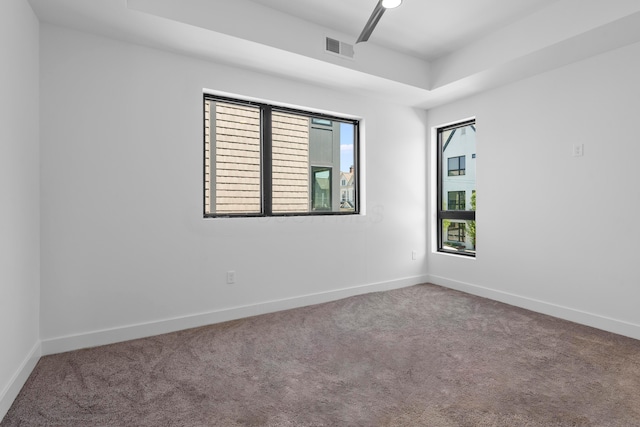 spare room featuring carpet floors, a tray ceiling, visible vents, and baseboards
