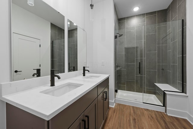 full bathroom featuring double vanity, a sink, wood finished floors, and a shower stall