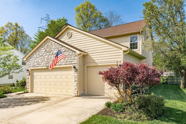 view of front facade with a front lawn, fence, stone siding, an attached garage, and driveway