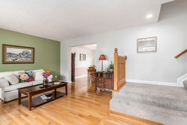 living area featuring a textured ceiling, stairway, baseboards, light wood-style floors, and recessed lighting