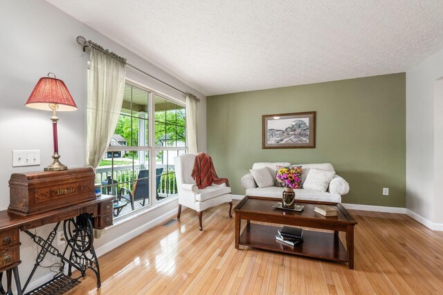 sitting room featuring wood-type flooring, a textured ceiling, visible vents, and baseboards